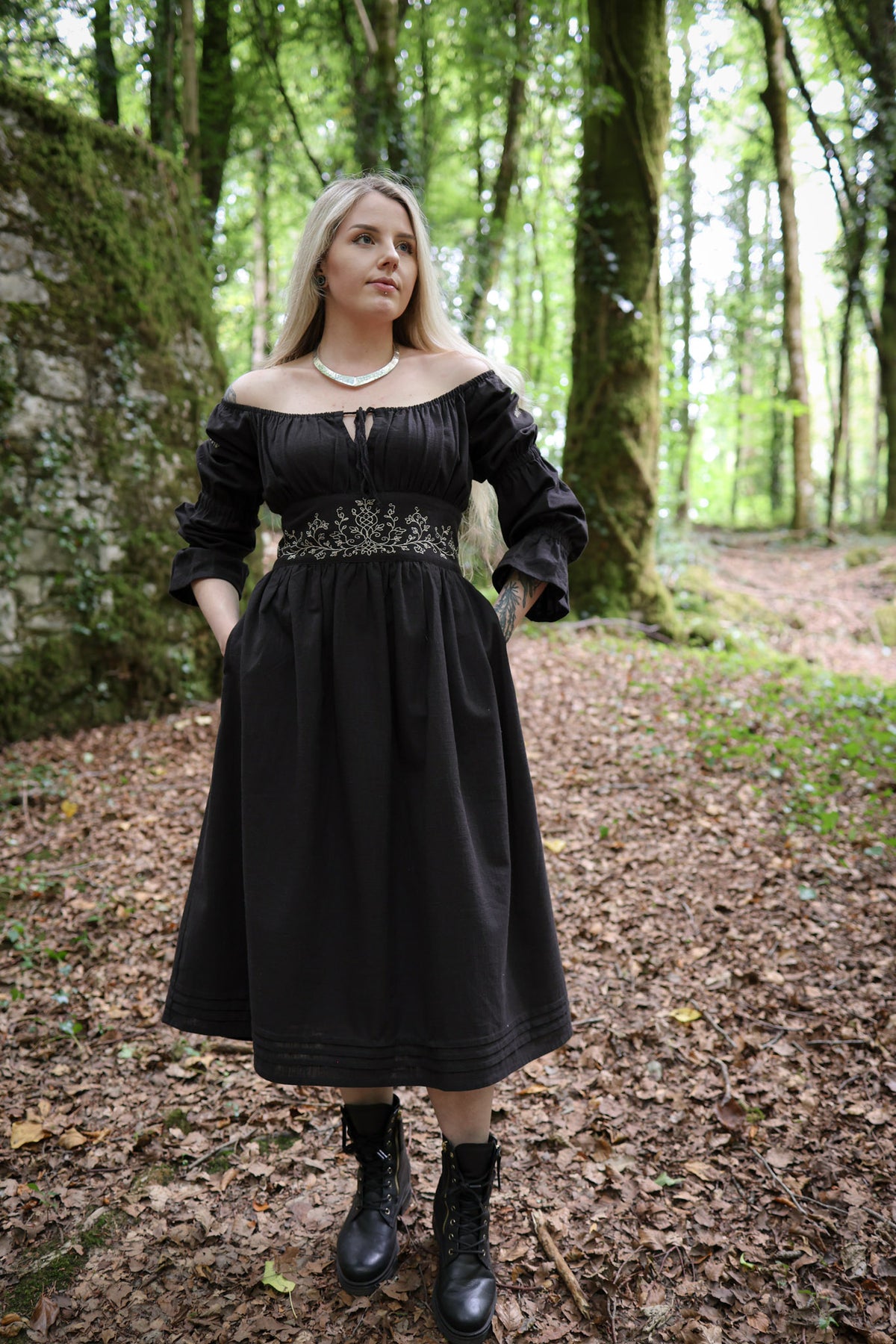 Black cotton embroidered midi dress with corset waist, off-shoulder neckline, pockets and folk-inspired styling in a woodland setting by irish designer Celtic Fusion