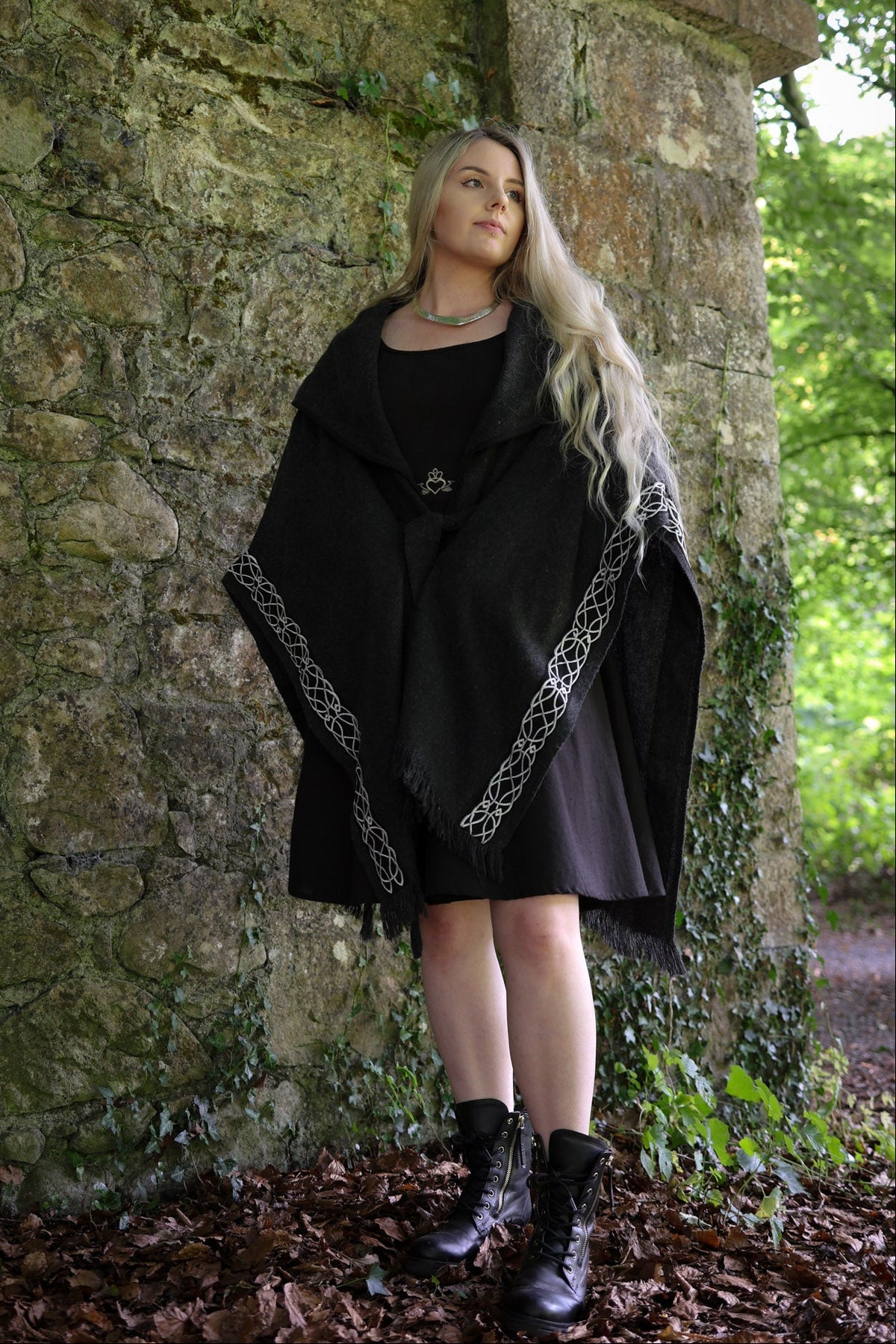 Woman wearing black folklore wool cape with Celtic knot embroidery in an old stone woodland setting by Celtic Fusion