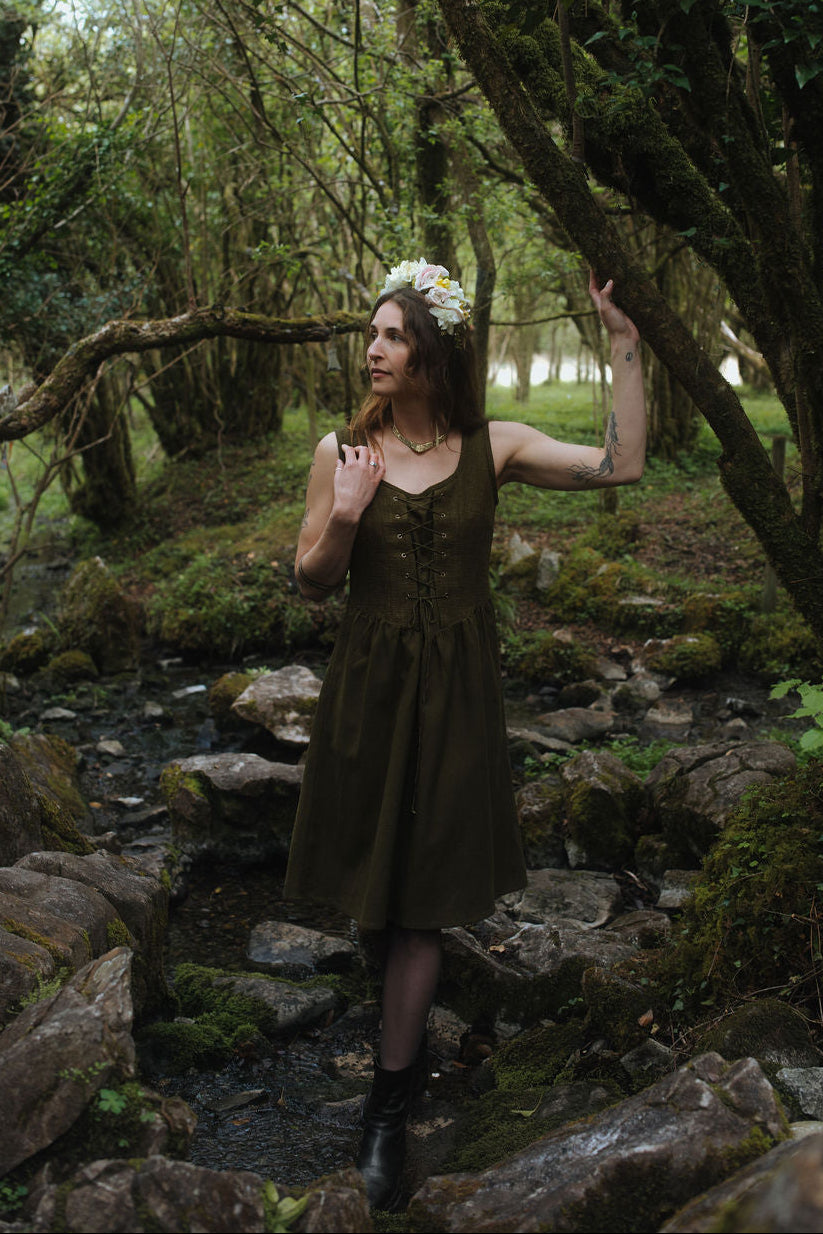 Rosemary Green Corset Dress, dark green folklore layering dress with pockets photographed beside a forest stream