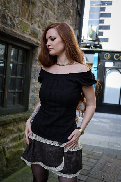 Black low waist tweed mini skirt with cotton lace trim and separate modesty shorts, styled with a black off shoulder top in an Irish street setting.