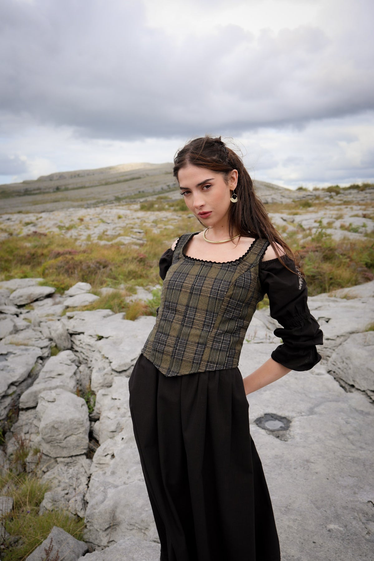 Folklore-inspired plaid tweed bodice with black lace trim, structured waist and layered black dress with sleeves in the Burren landscape created by Celtic Fusion designer
