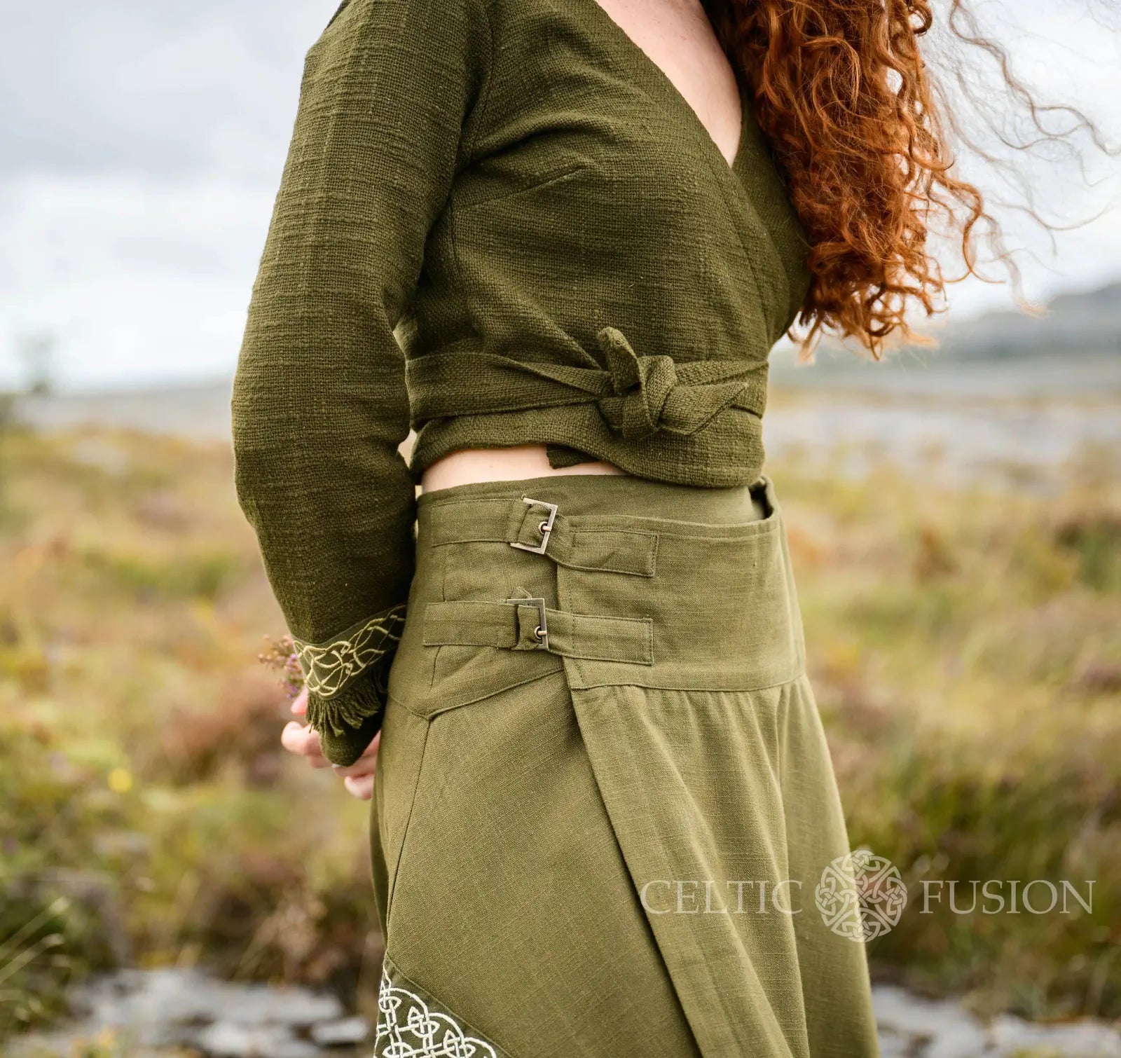 Close-up of the Elva green Celtic wrap cardigan showing its adjustable waist tie, textured heavy handwoven cotton fabric and embroidered knotwork cuff designed by Celtic Fusion