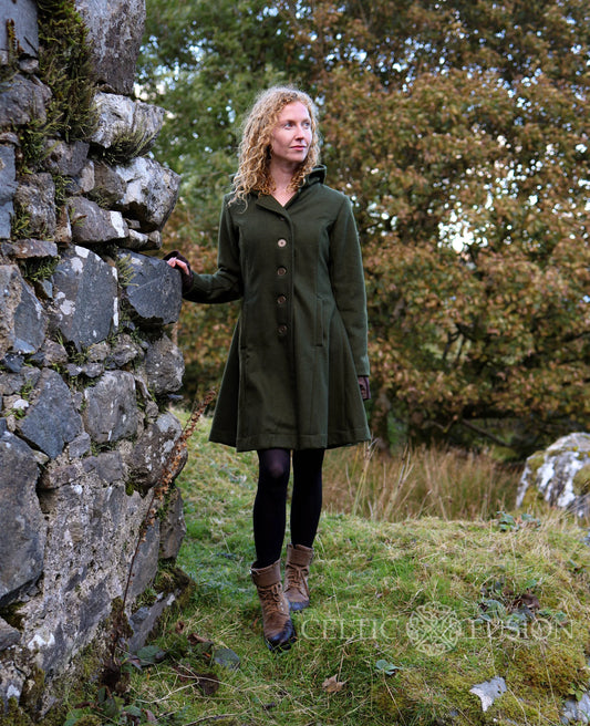 Dark green coat for women with a hood, midi length, and fitted silhouette, styled outdoors beside a stone wall.