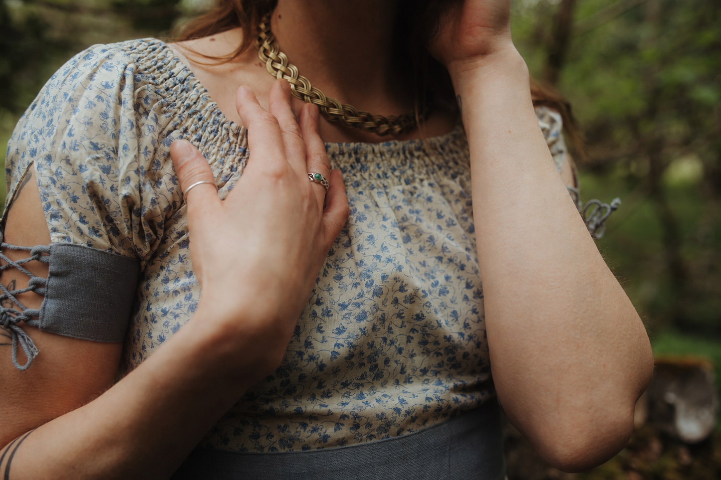 Close-up of the Forget Me Not Linen Dress showing the blue floral linen blend fabric, gathered neckline, grey waistband and Celtic torc necklace.
