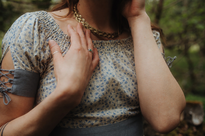 Close-up of the Forget Me Not Linen Dress showing the blue floral linen blend fabric, gathered neckline, grey waistband and Celtic torc necklace.