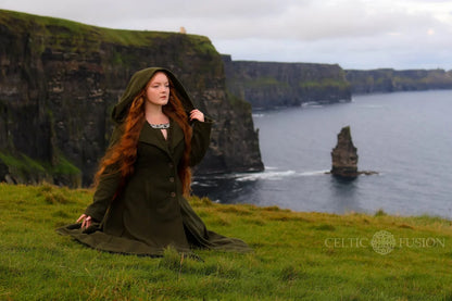 Woman wearing warm forest green hooded wool coat visiting the Cliffs of Moher in Ireland with full skirt and folklore inspired silhouette