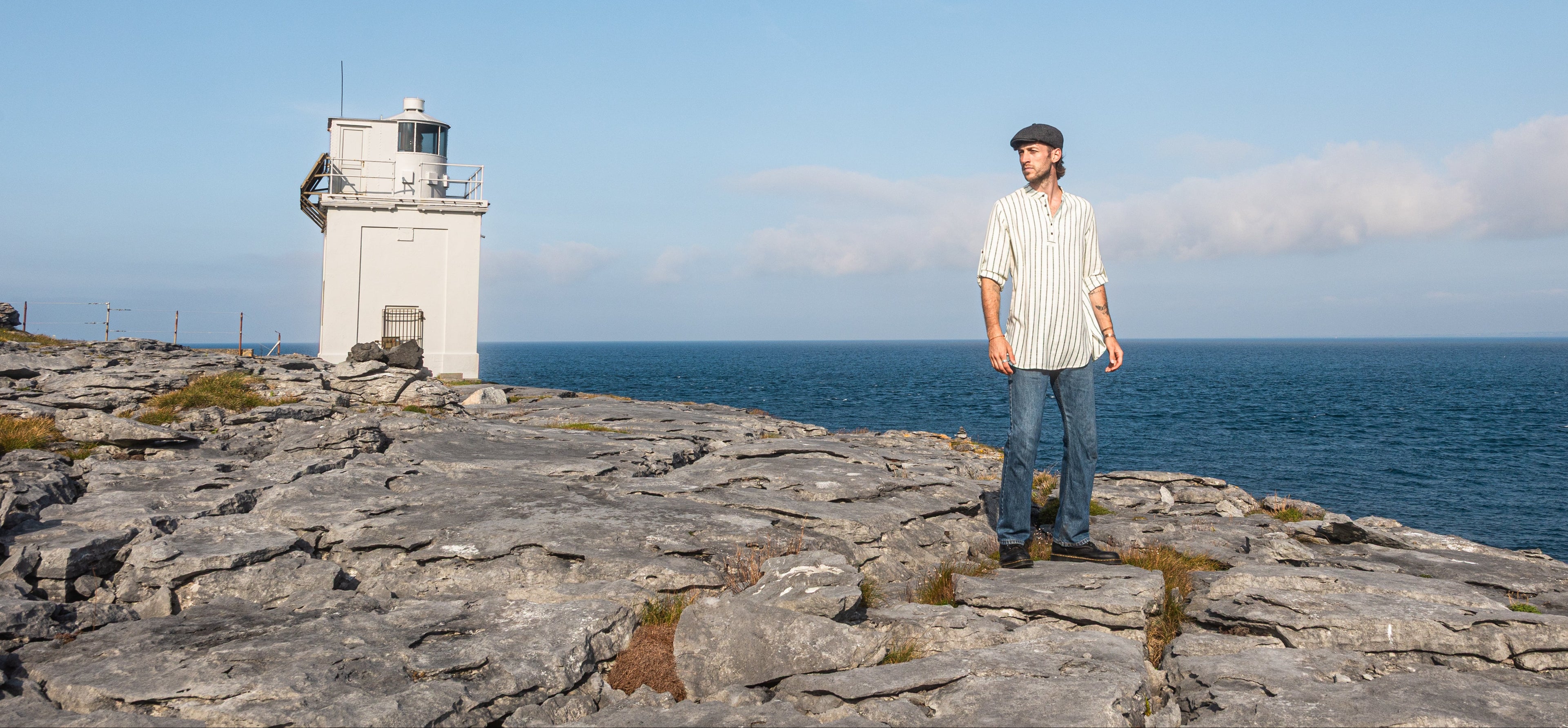 Irish clothing for men and Men’s Irish shirts by Celtic Fusion Design, striped collarless shirt styled with flat cap beside a lighthouse in Ireland