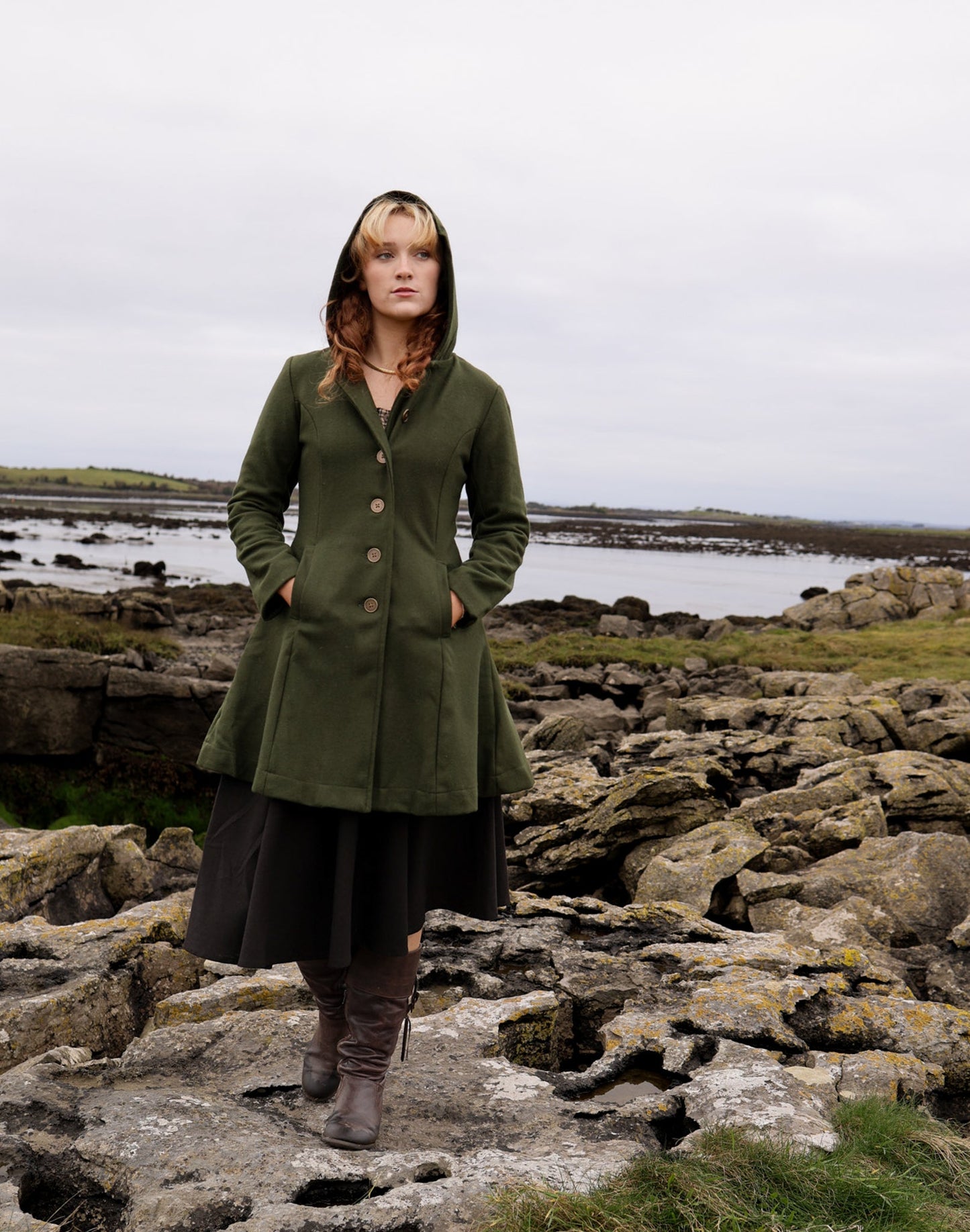 Midi green hooded coat for women in a wool blend, shown in a full front view on a rocky coastal landscape.