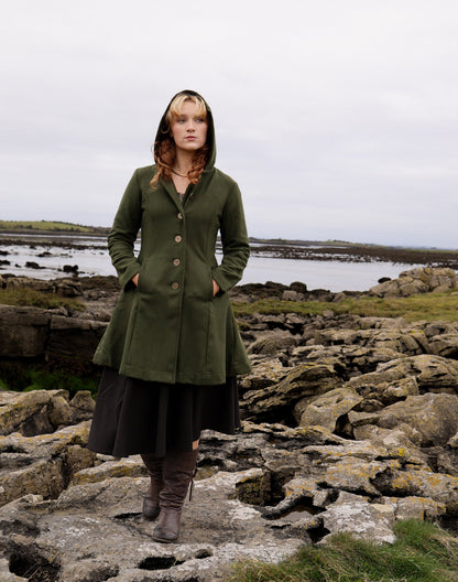 Midi green hooded coat for women in a wool blend, shown in a full front view on a rocky coastal landscape.