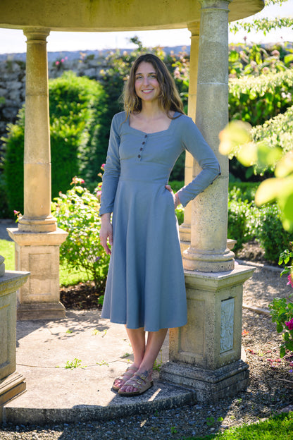 Pastel blue corset midi dress with pockets, long sleeves and a flowing circle skirt in a sunny garden.