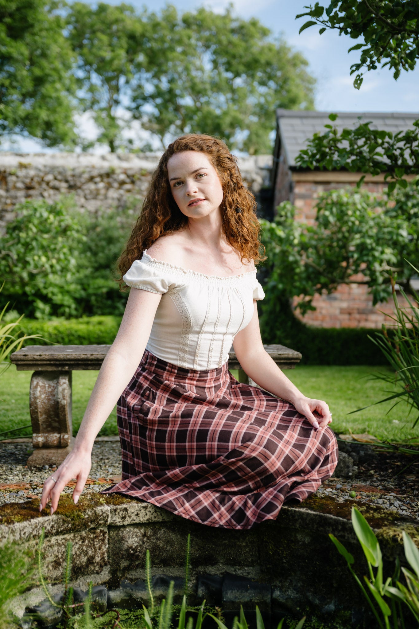 Soft cotton cottagecore check skirt with pockets, shown seated in a garden with an off-white fitted corset summer top.
