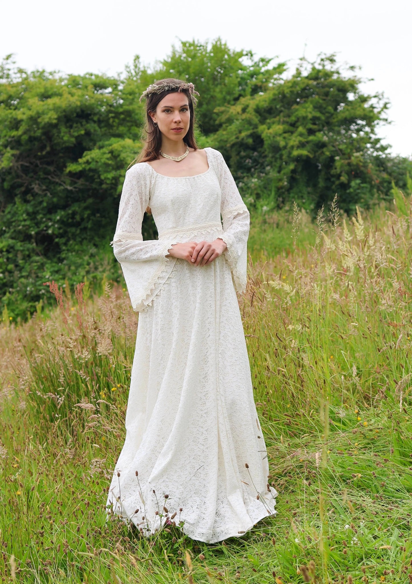 Sustainable cotton lace gown with bell sleeves, Bébhinn Boho Lace Wedding Dress shown outdoors in a meadow front view.