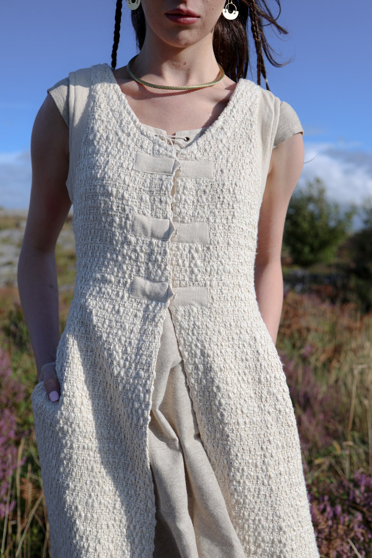 Textured cream corset overdress showing the sleeveless bodice, fabric loop fastenings and open-front construction.