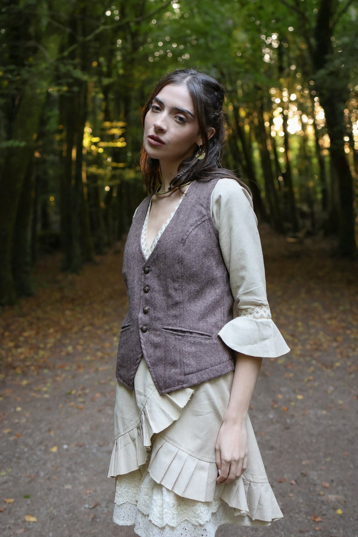 Women’s fitted tweed vest styled with natural linen dress and bell sleeves in forest setting