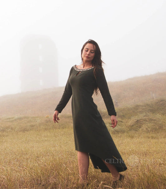 Green Celtic dress with Celtic knot embroidery, worn in an Irish landscape as an alternative wedding guest dress with high low skirt.
