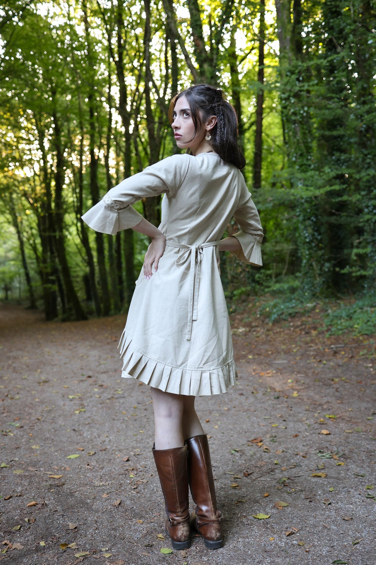 Back view of natural linen wrap dress showing tie waist, three-quarter bell sleeves and pleated hem detail.