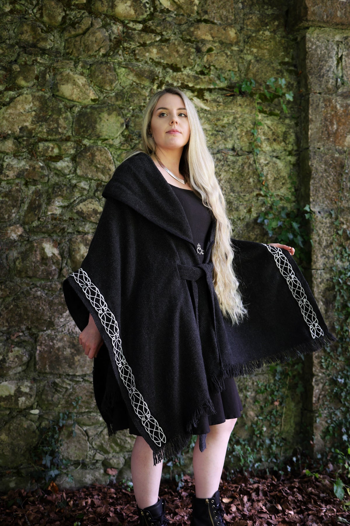 Woman wearing black Druid Celtic wool cape with mystical hood, belt and Celtic knot embroidery outdoors