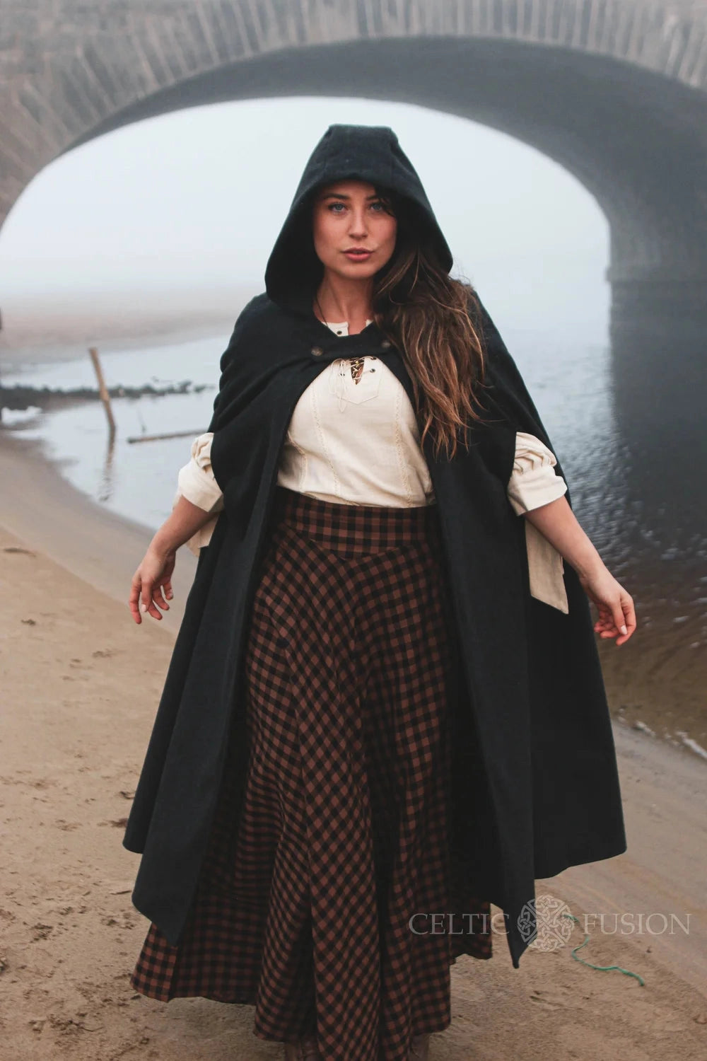 Woman wearing mystical black folklore wool cloak with hood and sleeveless poncho-style design in an outdoor setting
