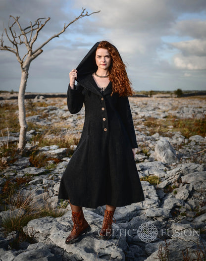 Woman wearing black long hooded wool coat with full skirt and dramatic fairytale-inspired silhouette in the Burren by Celtic Fusion Design