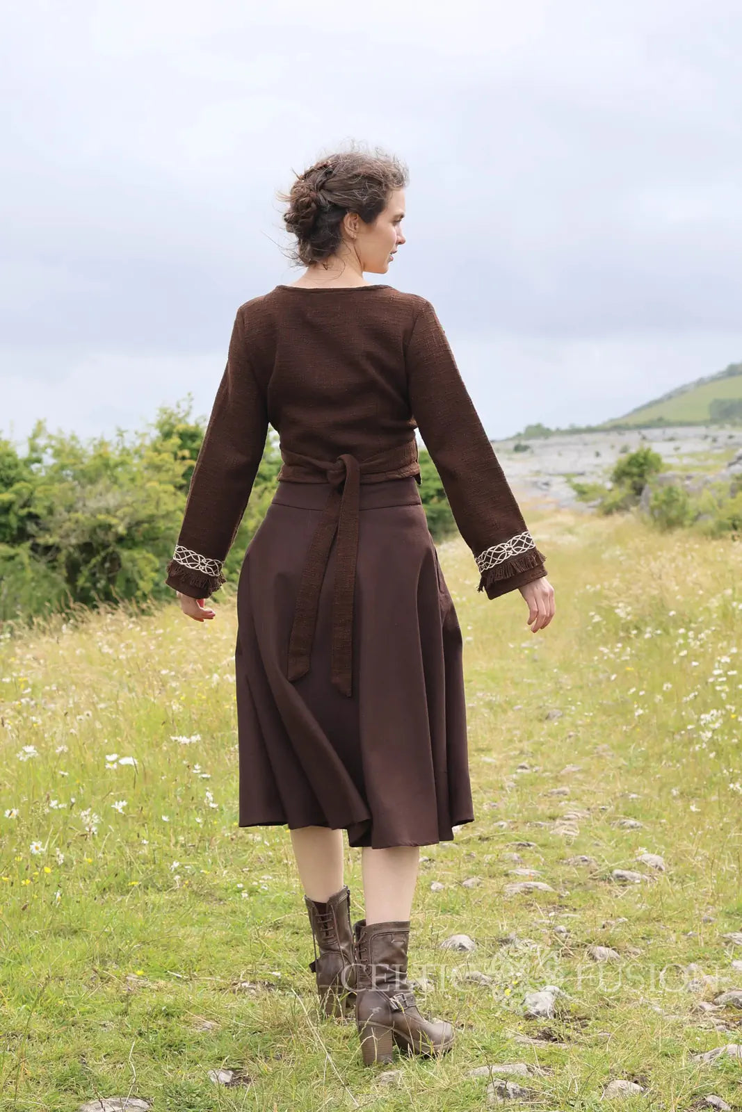 Back view of the Elva brown Celtic wrap cardigan showing the waist ties, long sleeves and Celtic embroidered cuffs with a flowing brown midi skirt.