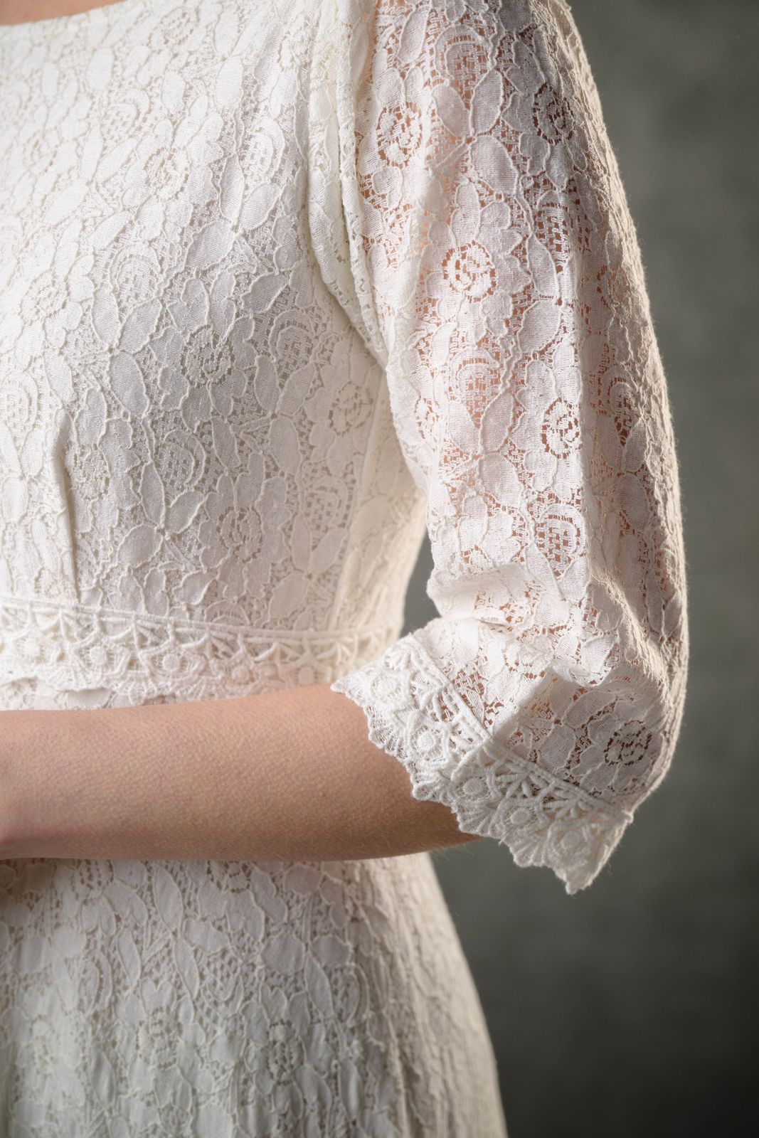 Close-up of natural cotton ivory lace bridal dress showing floral lace sleeve, scalloped cuff and delicate waist trim