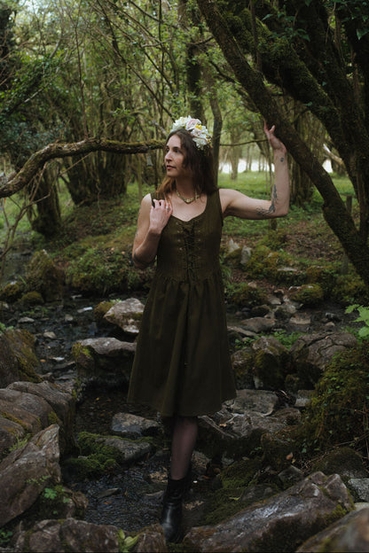 Rosemary Green Corset Dress, dark green folklore layering dress with pockets photographed beside a forest stream