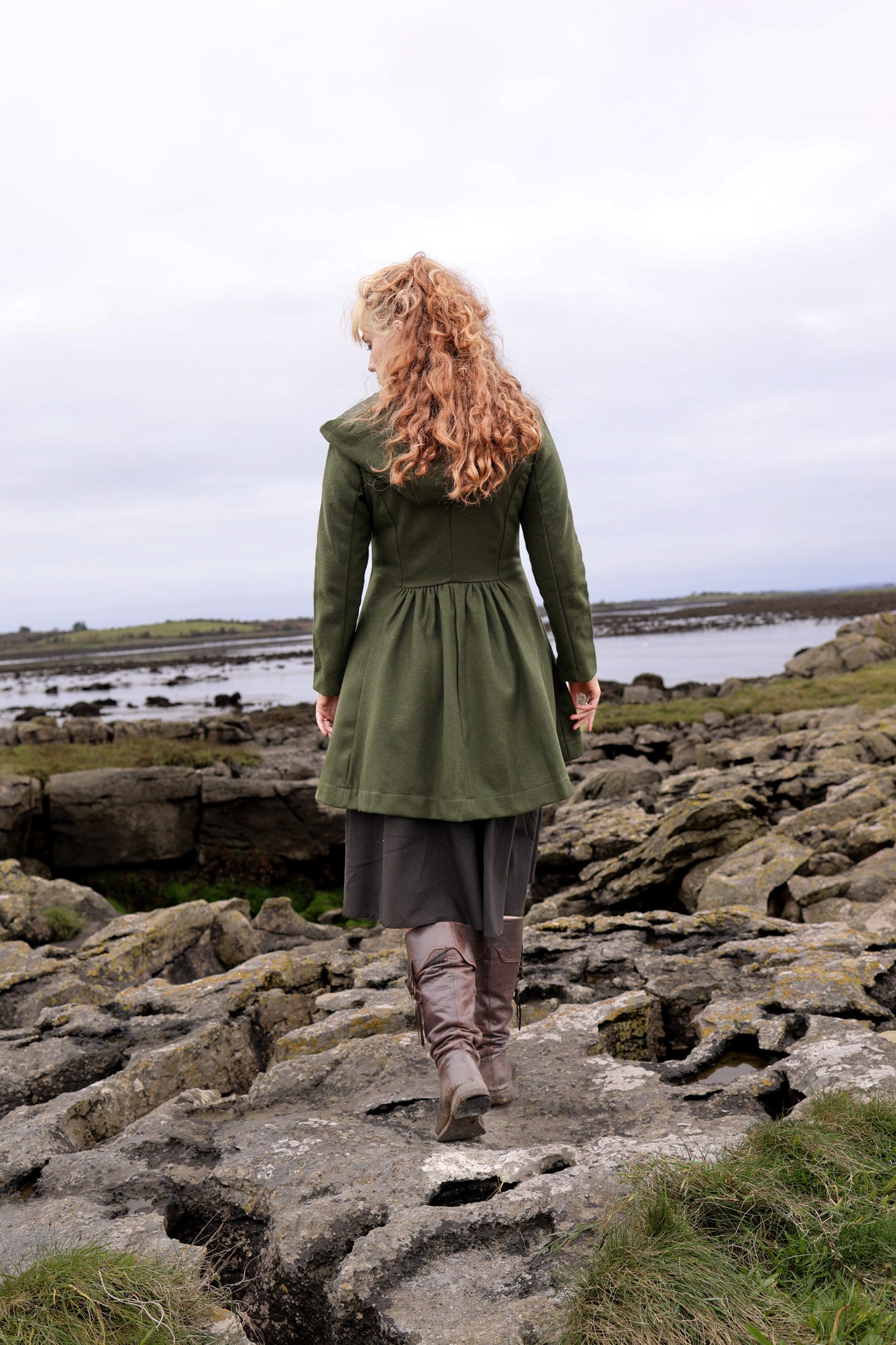 Back view of a dark green hooded coat for women with a softly fitted waist and flared midi skirt shape.