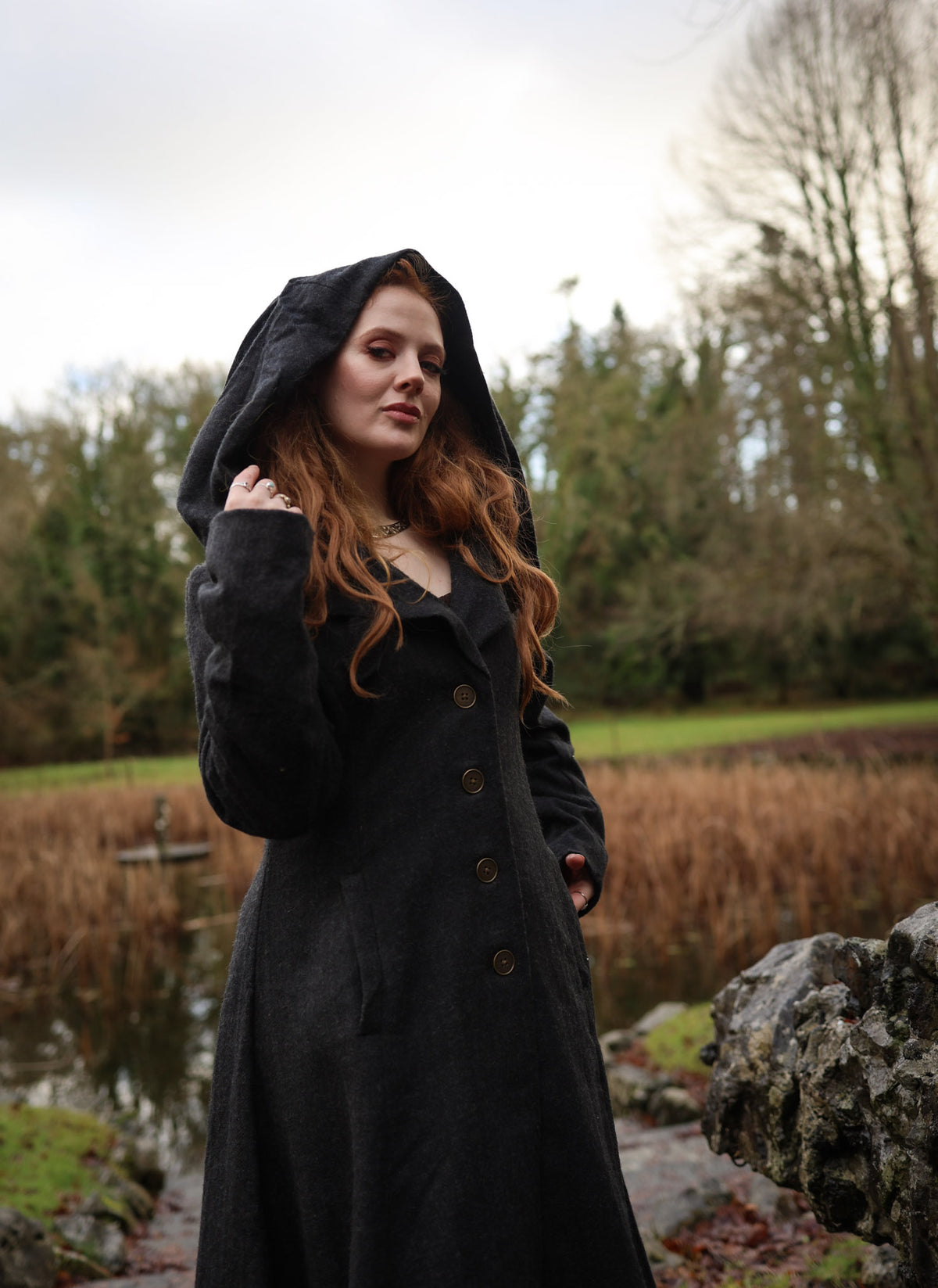 Close-up of black hooded wool coat with dramatic oversized hood, tailored bodice and single-breasted buttons