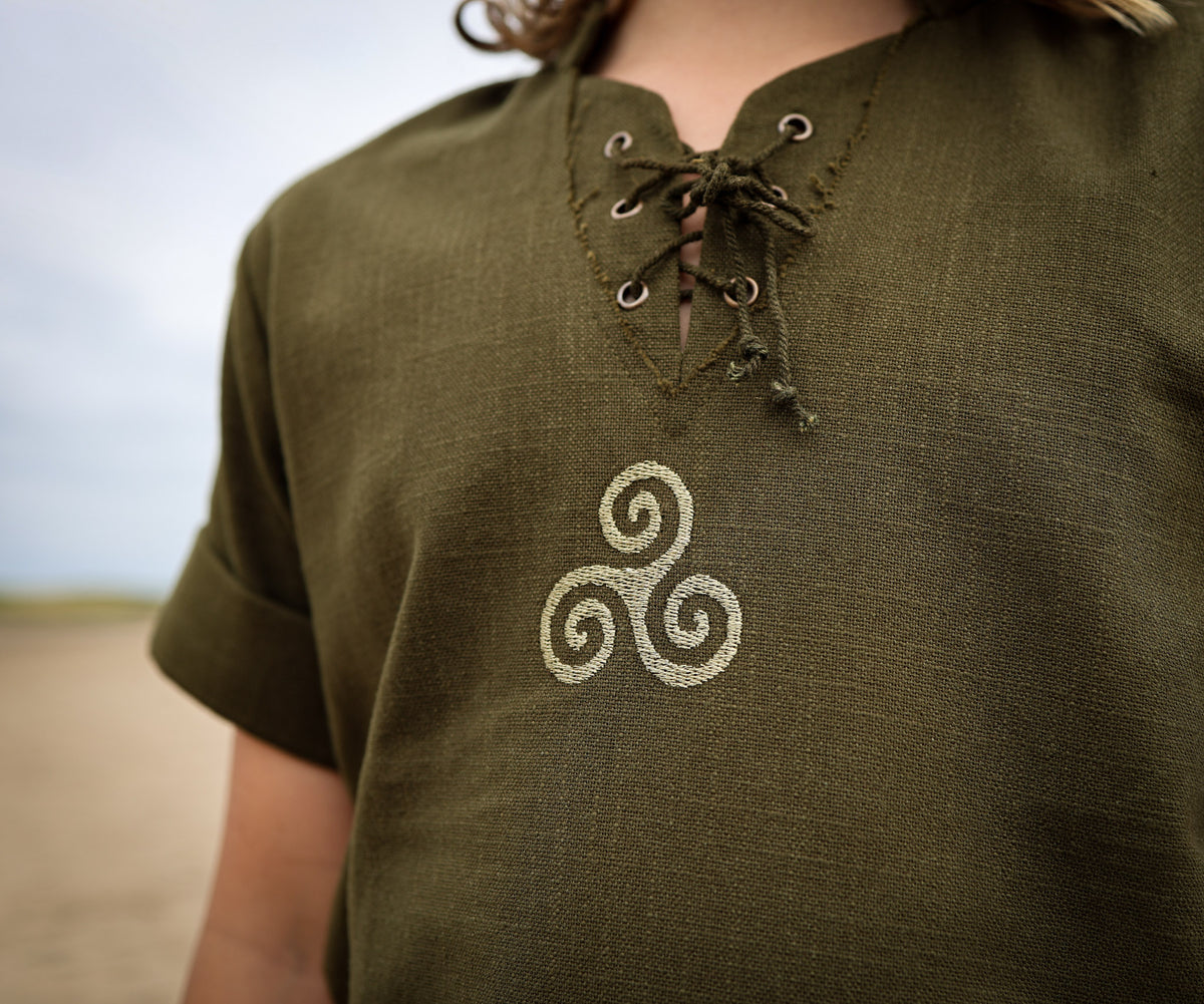 Close-up of green boys Celtic shirt showing embroidered Triskele symbol and traditional lace-up neckline.