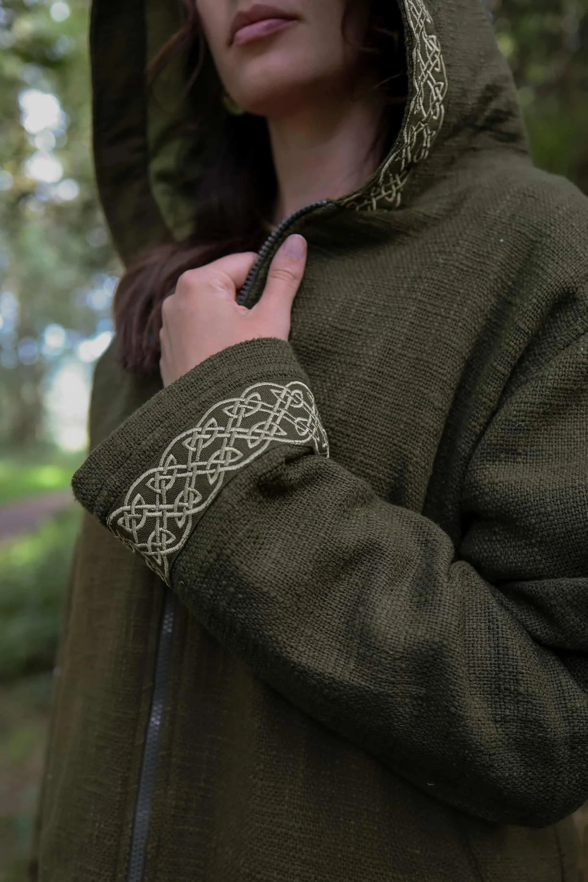 Close-up of olive green Celtic jacket showing embroidered knotwork detail on the cuff and hood edge.