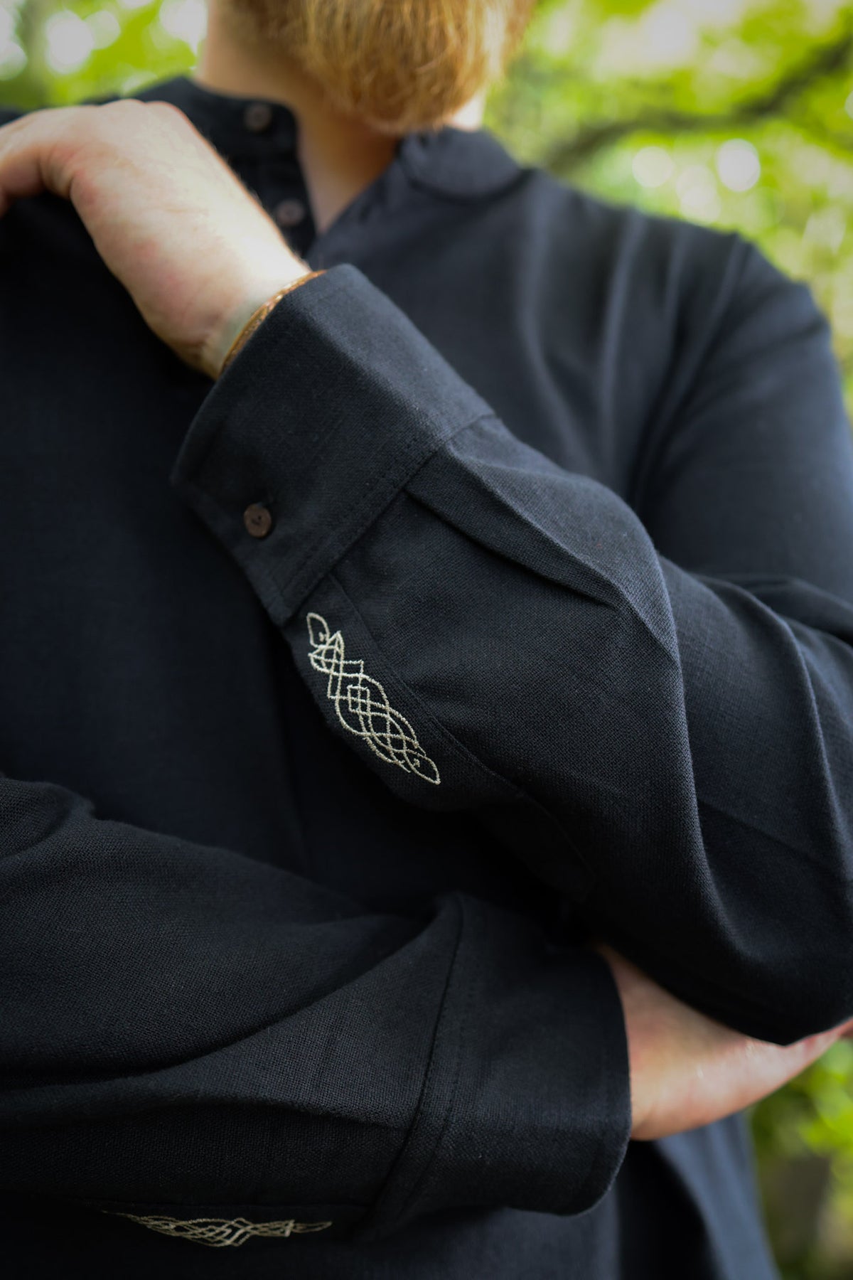 Close-up of the Dubh shirt showing fine-line Celtic knotwork embroidery on the black cotton sleeve cuff.