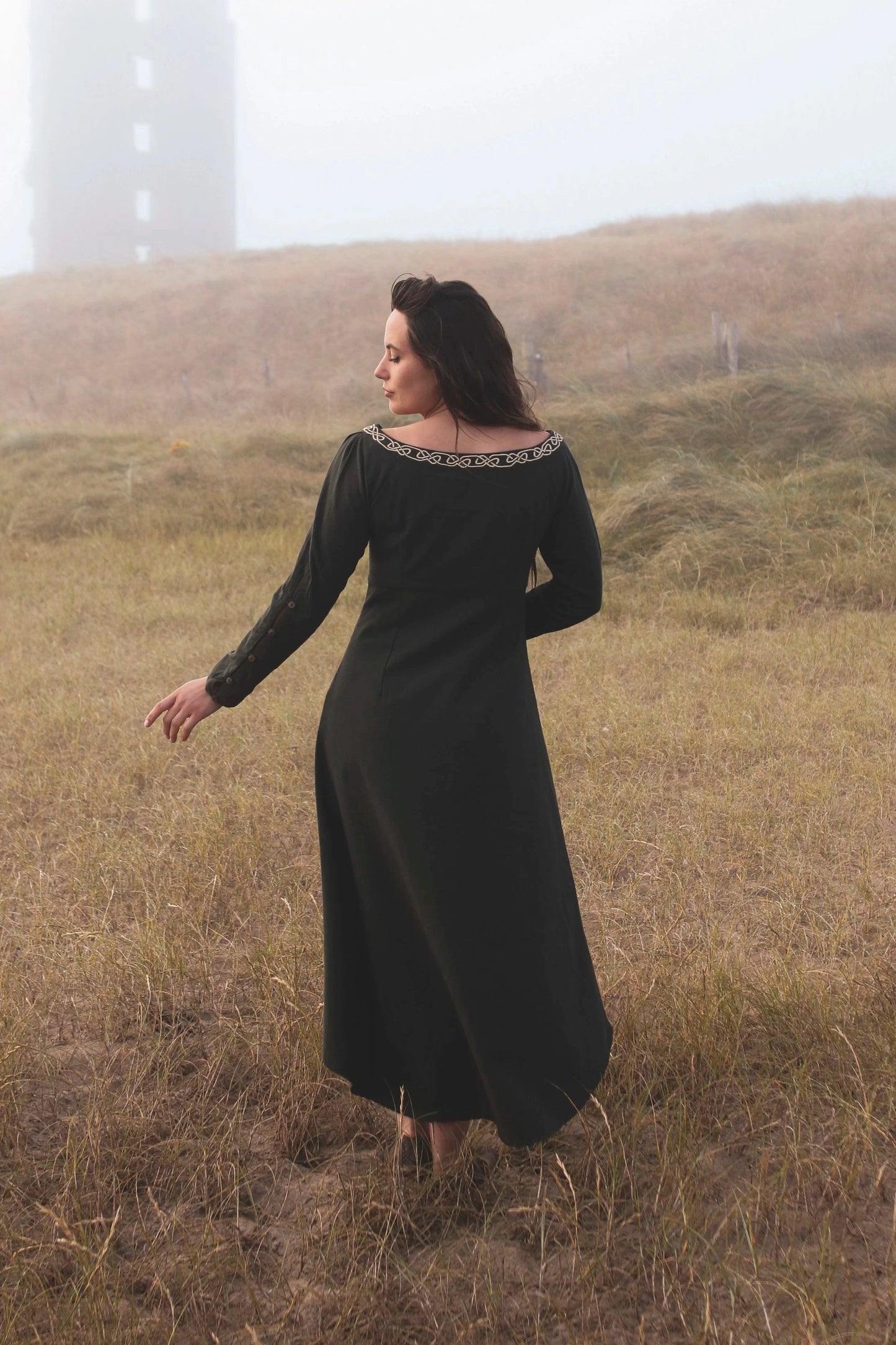 Back view of green Celtic dress with long sleeves and flowing silhouette, an alternative wedding guest dress with high low skirt and folklore styling.