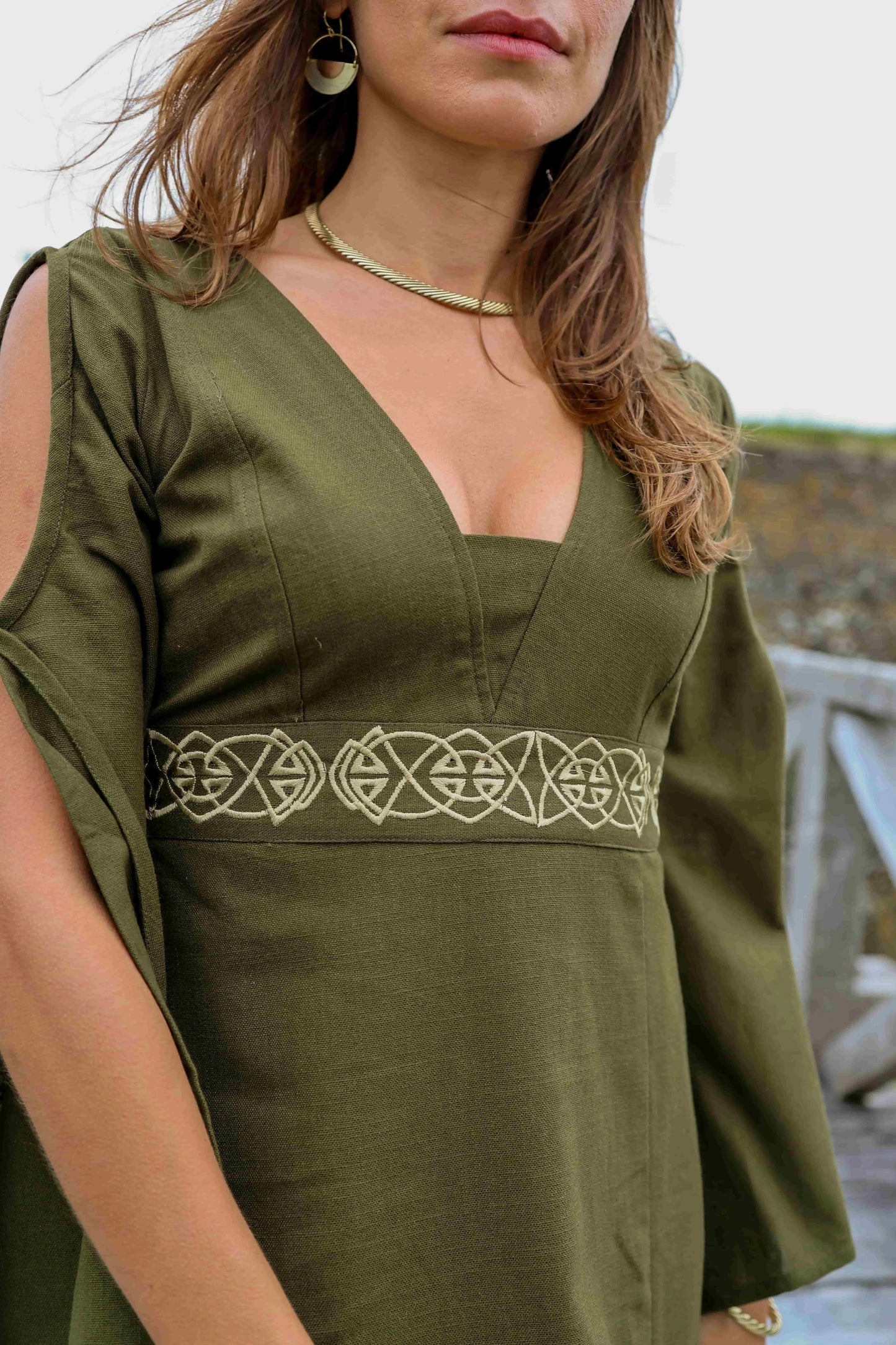 Close-up of the Maeve Celtic Dress showing deep V neckline, olive green cotton slub fabric and Celtic knot embroidery at the waist.