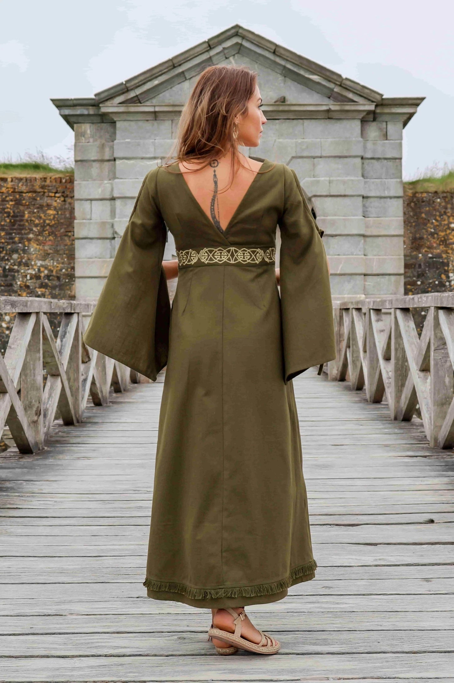 Back view of the Maeve Celtic Dress, green Celtic maxi dress with flowing bell sleeves, deep V back and embroidered Celtic waist detail.