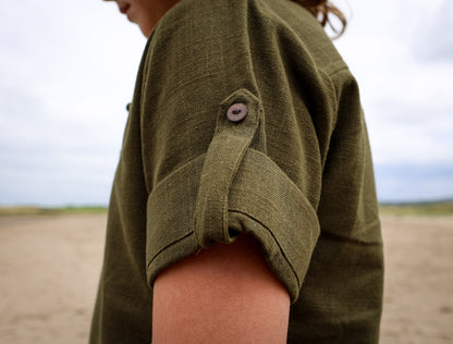 Close-up of olive green boys folklore shirt by Celtic Fusion clothing showing roll-up sleeve with button fastening and natural fabric texture.