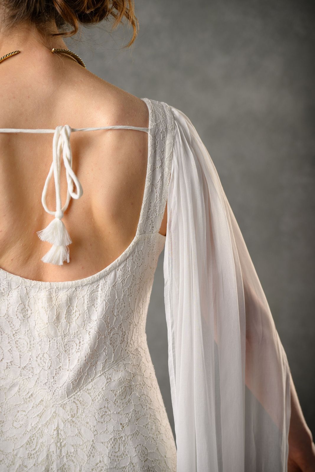 Close-up of ivory lace Irish wedding dress back with tie fastening, tassel detail and soft chiffon drape sleeve