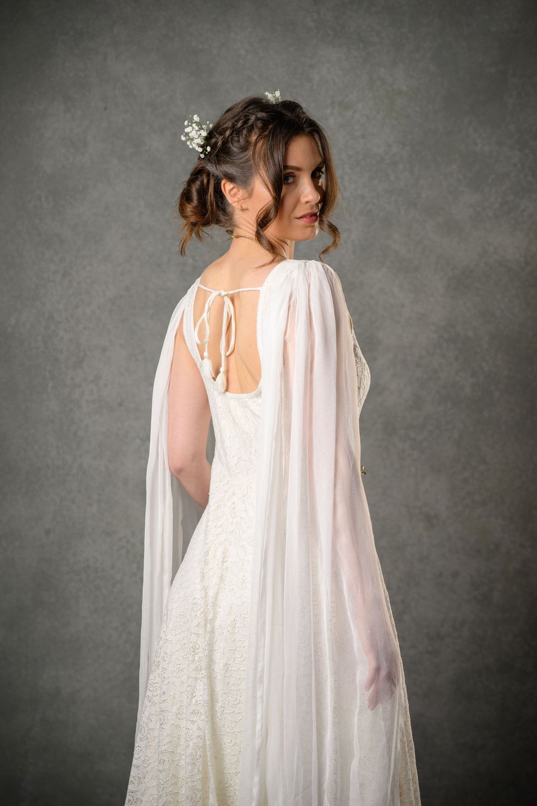 Ivory bridal gown with open back, shoulder tie detail, flowing chiffon sleeves and lace skirt shown from the back