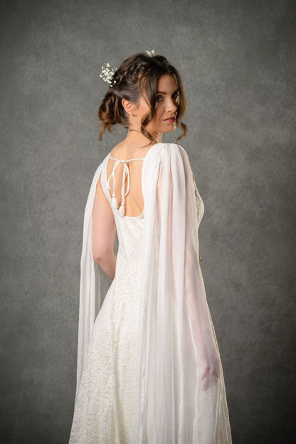 Ivory bridal gown with open back, shoulder tie detail, flowing chiffon sleeves and lace skirt shown from the back