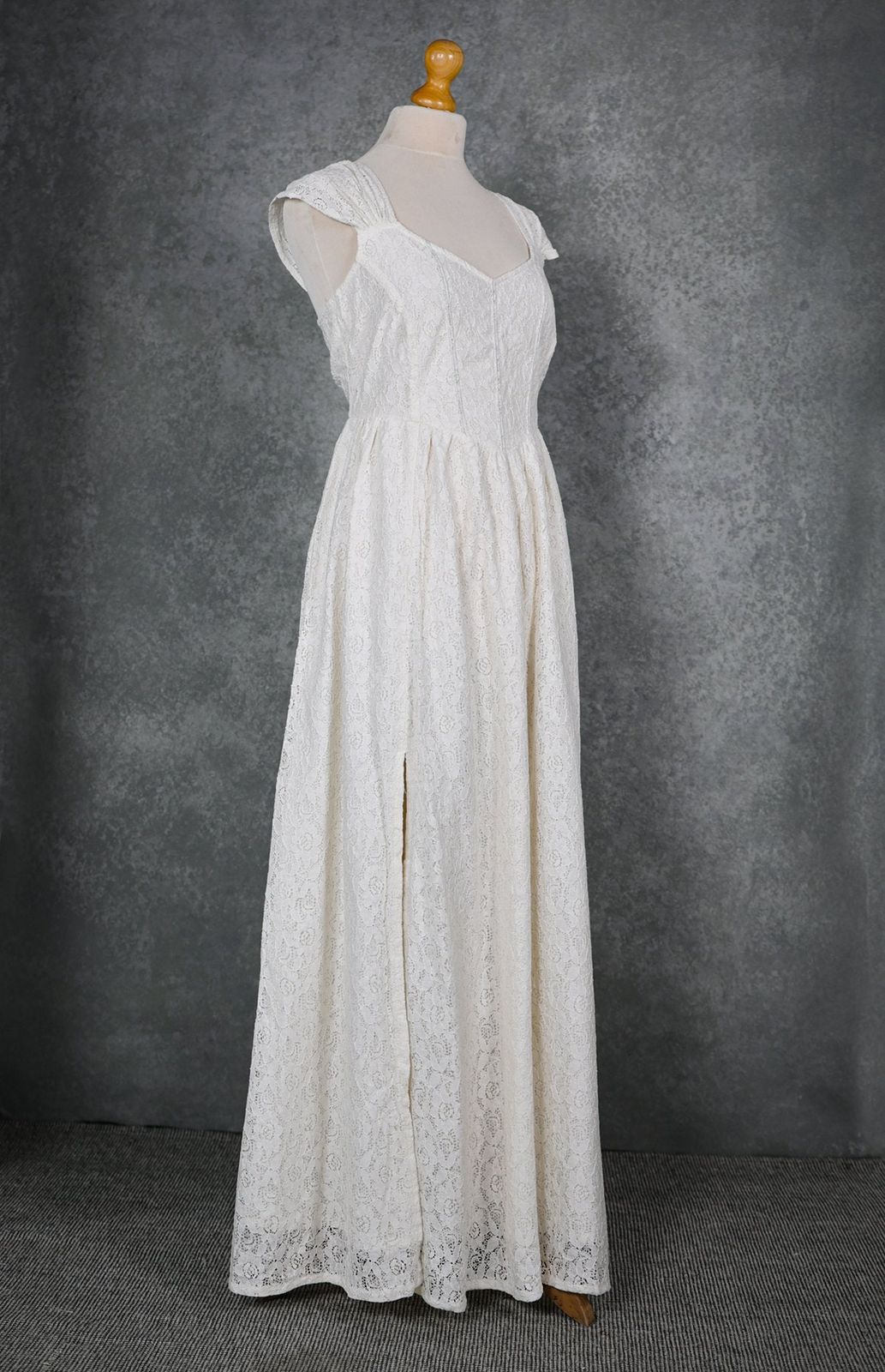 Ivory floral cotton lace wedding dress on mannequin with corset bodice, gathered shoulder straps and front slit