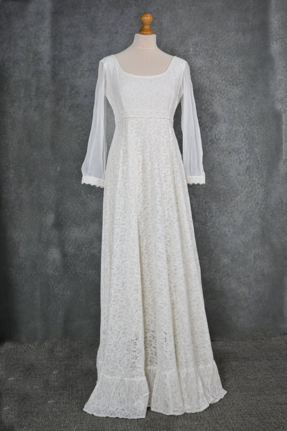 Ivory cotton lace sleeved wedding dress on mannequin with scoop neckline, empire waist detail and flowing hem frill