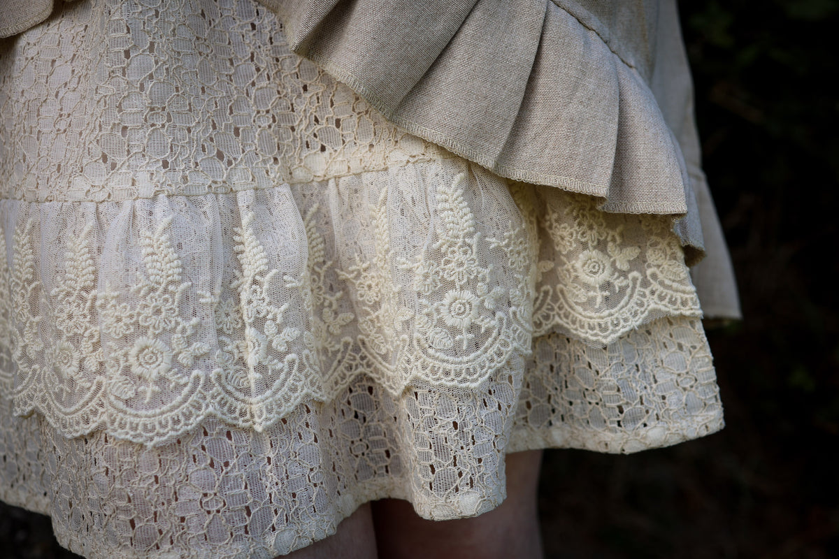 Close-up of layered cotton lace skirt beneath the natural linen wrap dress, showing floral embroidery and lace texture.