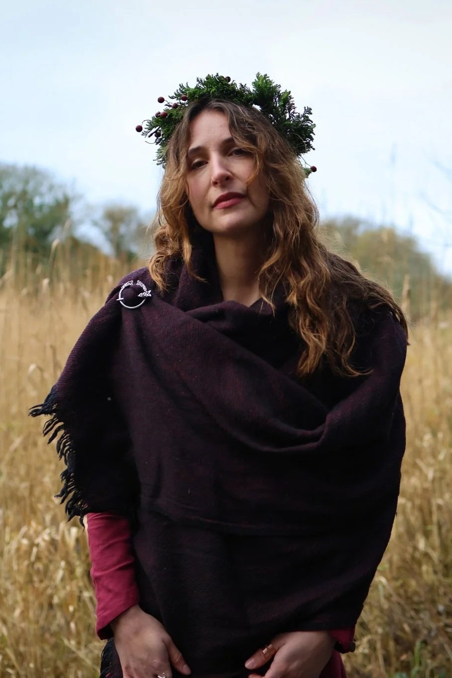 Maroon and black handwoven shawl fastened with silver Trinity brooch in an outdoor folklore setting