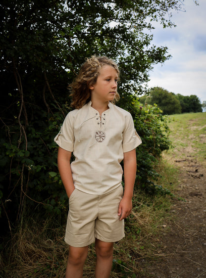 Boy wearing natural cotton Vegvisir Celtic shirt with short roll-up sleeves and earthy medieval inspired styling outdoors