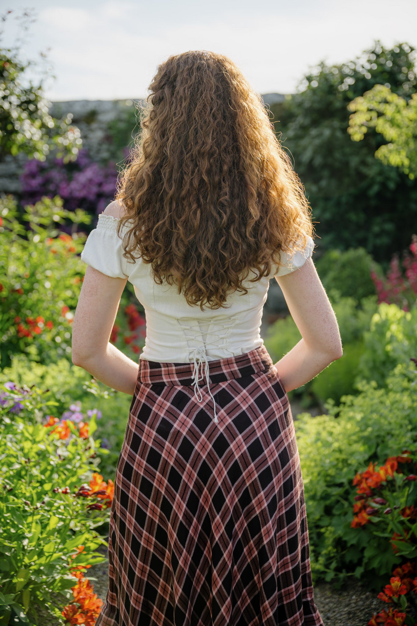 Back view of a pink and brown plaid midi skirt with a flowing A-line silhouette, styled with a corset-back cotton top.