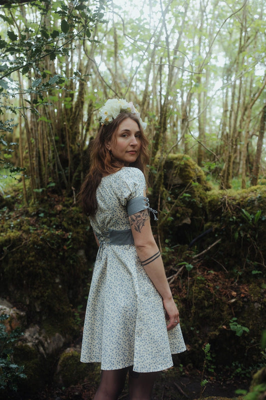 Blue floral linen blend dress with smocked neckline, corset back waist detail and lace-up sleeves, styled as a romantic garden party wedding guest dress.