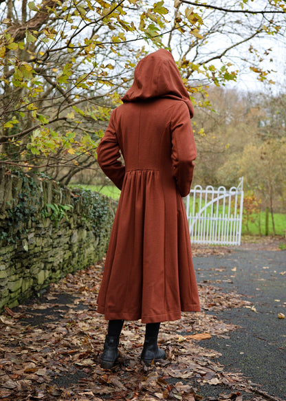 Back view of rust hooded maxi coat showing oversized hood, fitted waist and full flowing skirt
