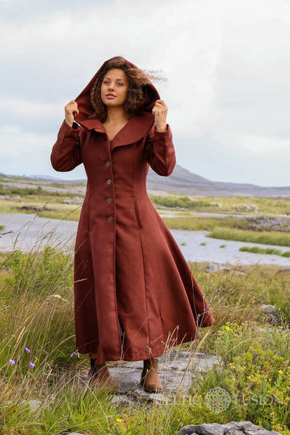 Woman wearing rust hooded maxi wool coat with oversized hood and full skirt in a wild Irish landscape