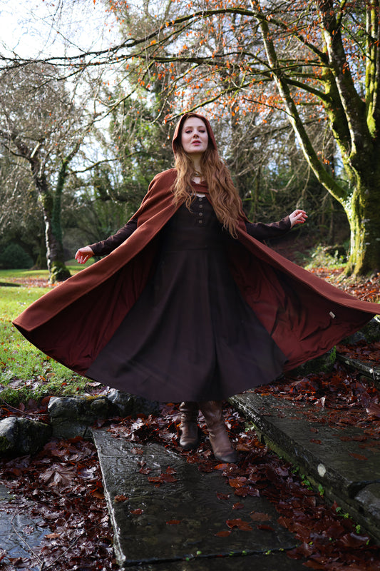 Woman wearing rusty red hooded wool cloak with maxi length, open sides and folklore-inspired silhouette by celtic fusion design