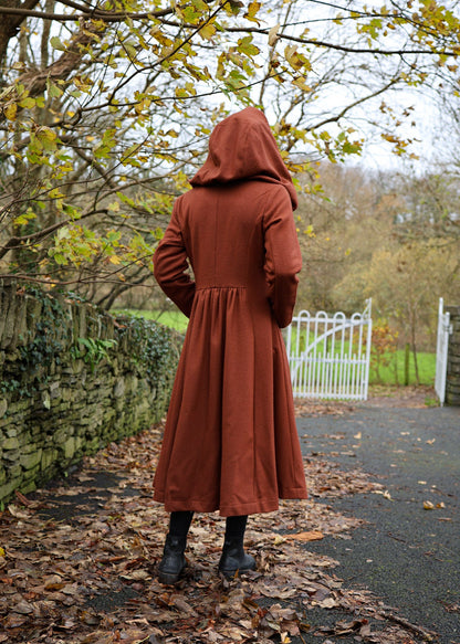 Back view of rearthy rusty red hooded wool coat showing cinched waist and full-length flowing skirt