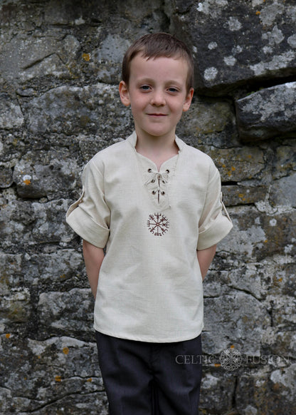 Young boy wearing off-white Celtic medieval shirt with Vegvisir embroidery and lace-up neckline against stone wall